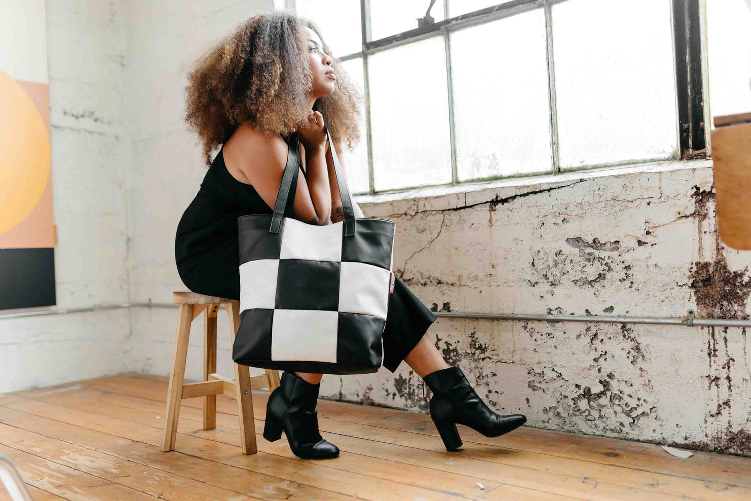 Model holding a black and white vegan checker tote while gazing out a window