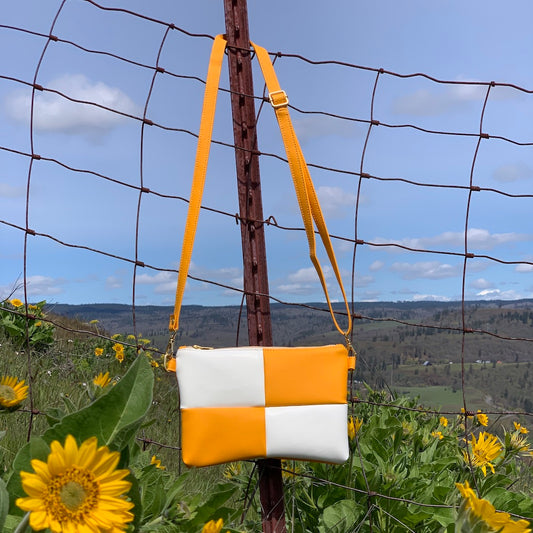 Handmade yellow and white checker crossbody bag hanging on a fence among yellow flowers