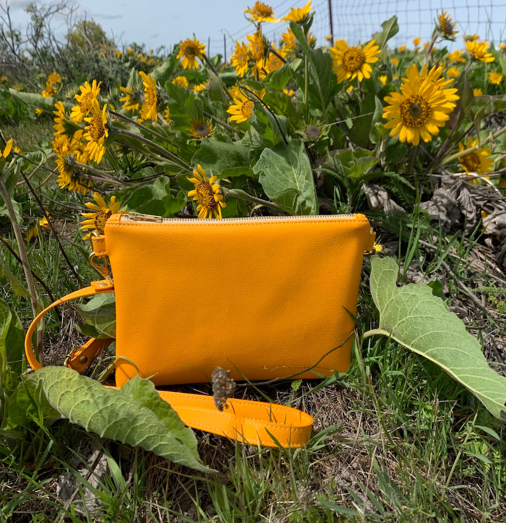 Bright marigold vegan cactus leather crossbody bag placed in front of yellow flowers