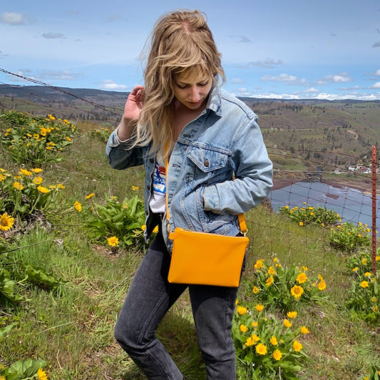 Woman gazing down at handmade marigold vegan leather crossbody bag